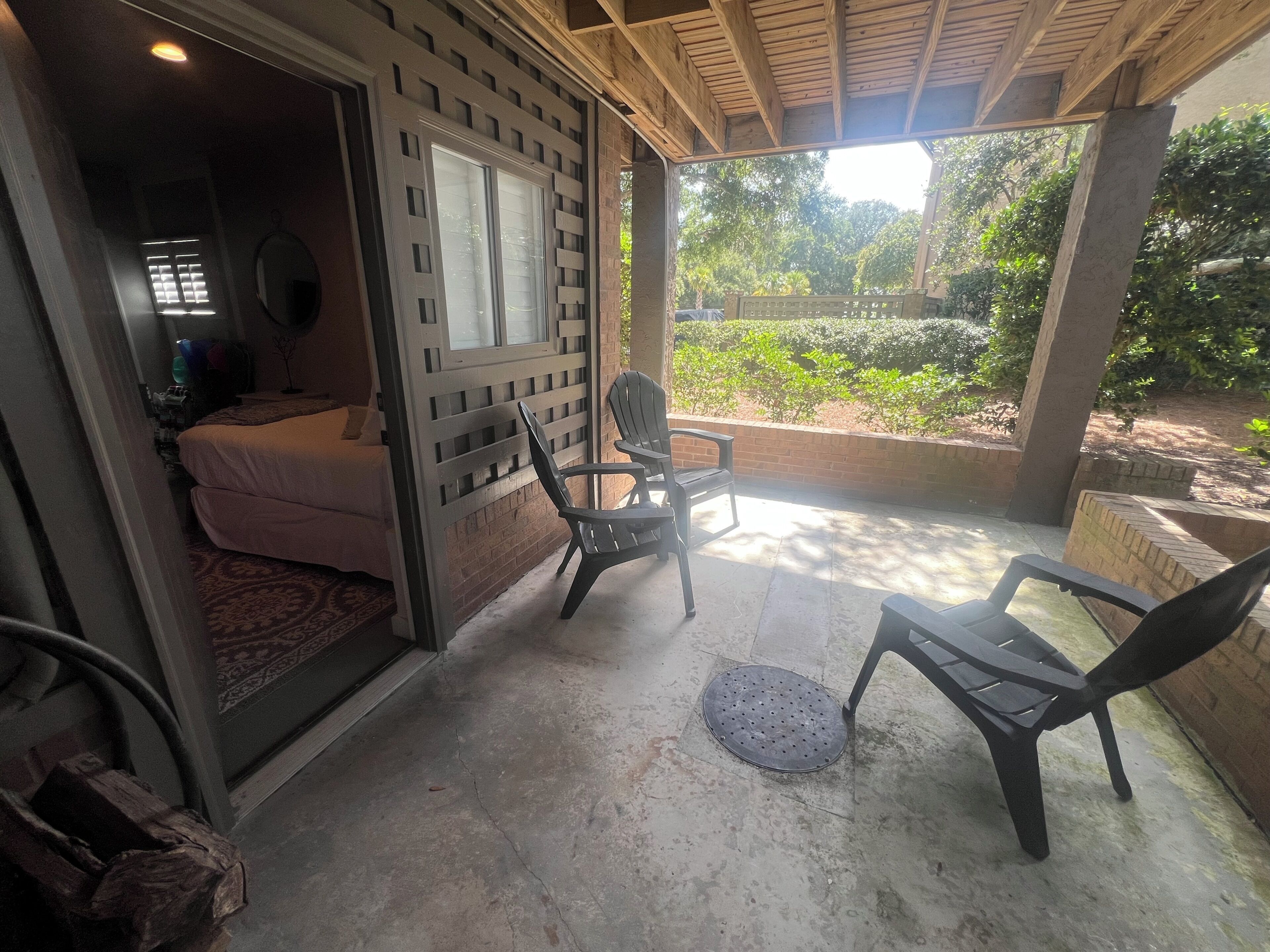 A room with a bed, a window, and a view of greenery outside. There are two chairs and a small table.