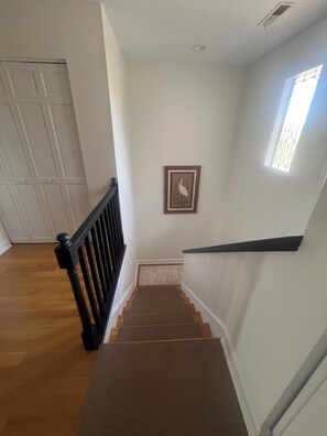 A staircase with a wooden handrail and carpeted steps leading to a landing with a framed picture. - Waterfront Marina Condo & Breathtaking Sunset Views & Walk to Dining (Johns Island)