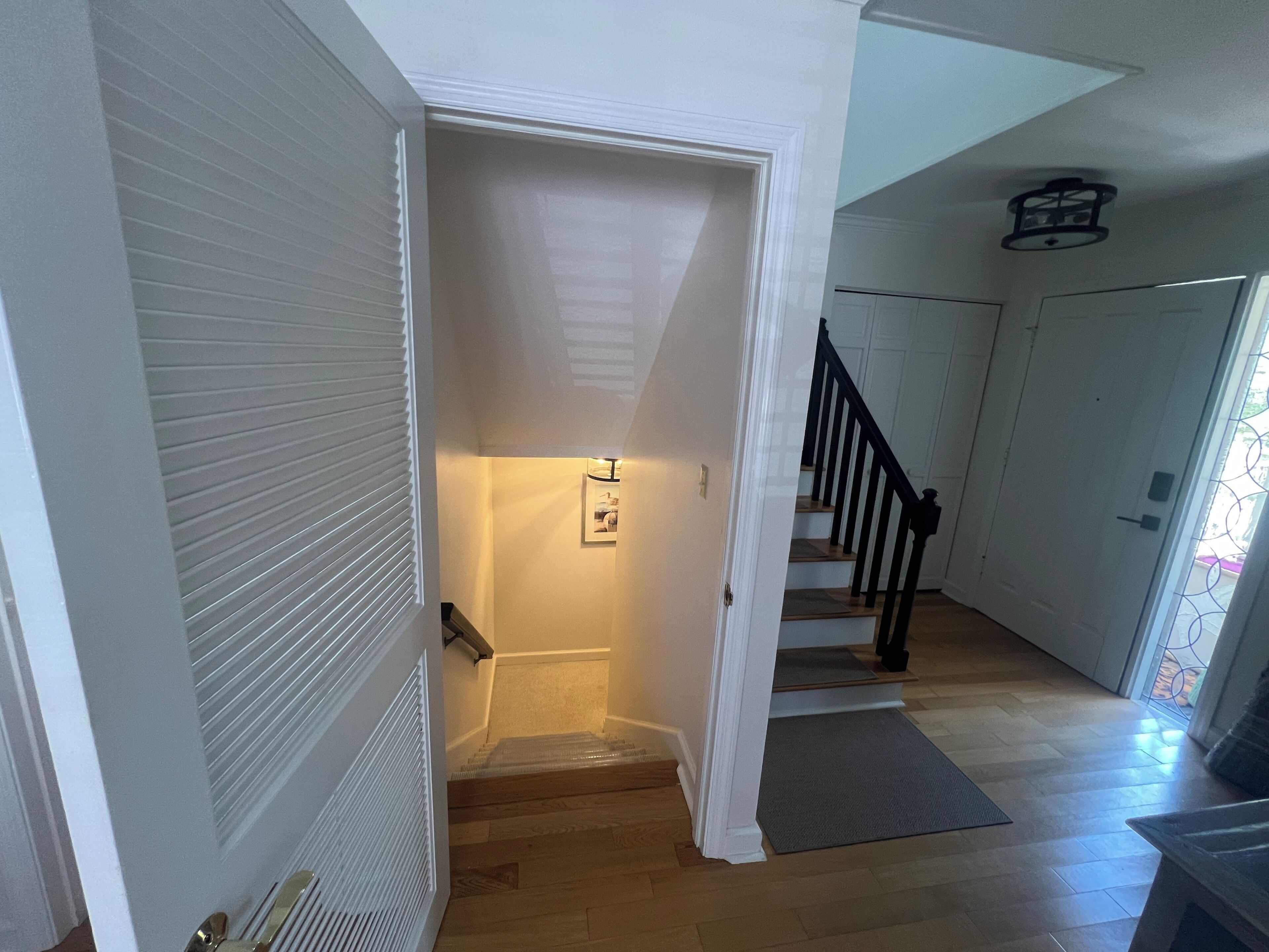 Un pasillo con piso de madera, una puerta blanca y una escalera con barandales negros.