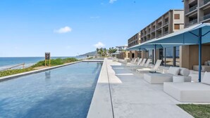 Ein Poolbereich mit Liegestühlen, Blick auf das Meer und ein Gebäude mit Balkonen.