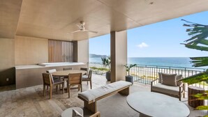 Ein moderner Außenbereich zum Entspannen mit Essplatz, Stühlen, einer Bank und einer Sitzecke, mit Blick auf Strand und Meer.