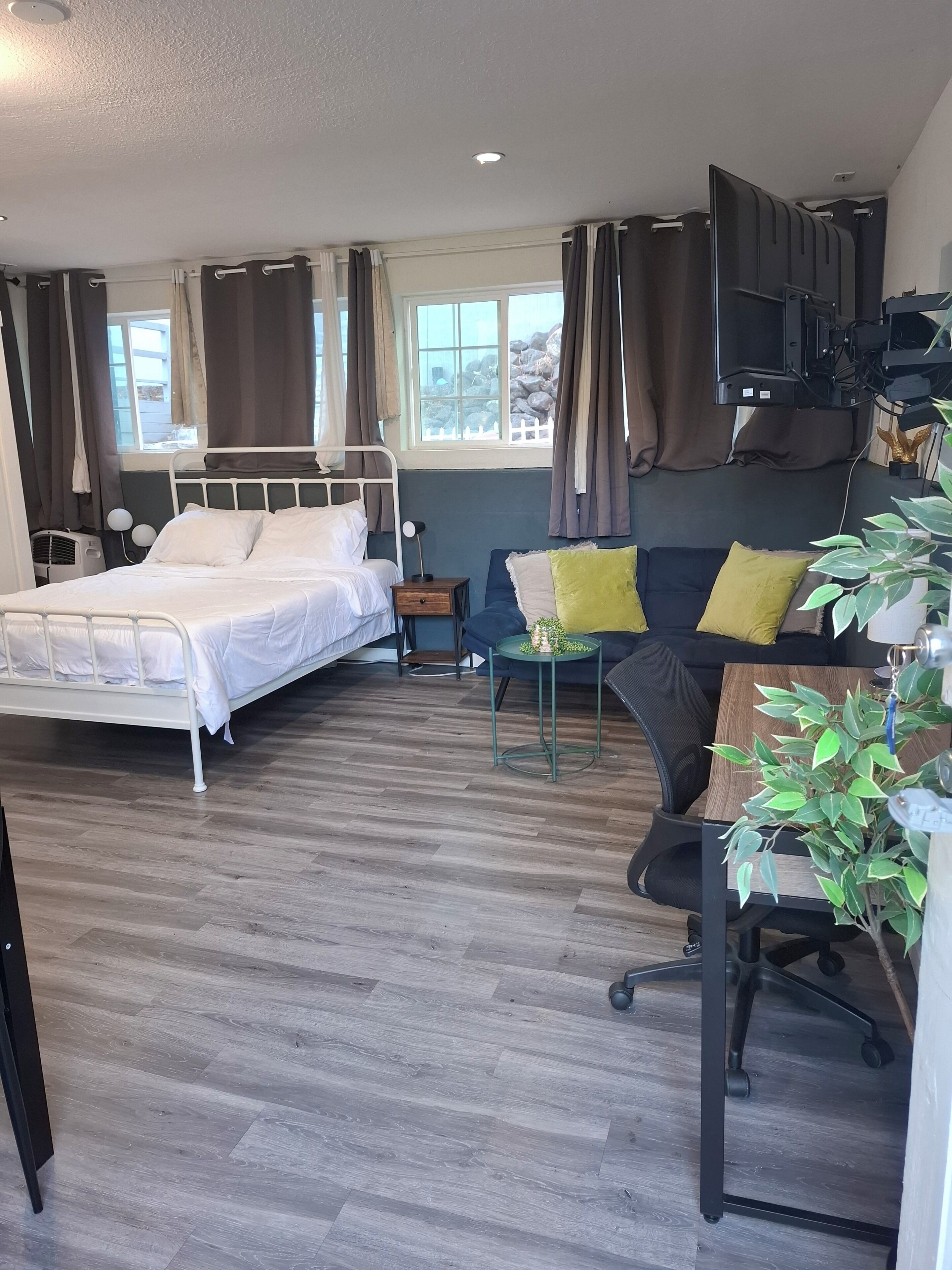 A hotel room with a bed, a sofa, a small table, a TV, and a window with curtains.
