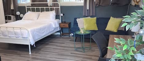 A hotel room with a bed, a sofa, a small table, a TV, and a window with curtains.