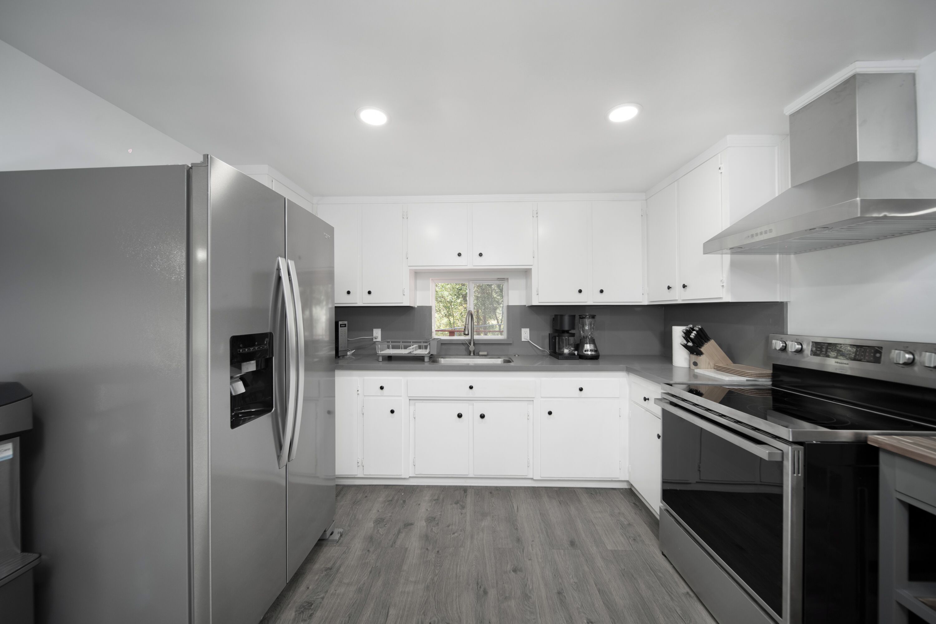 Una cocina moderna con armarios blancos, electrodomésticos de acero inoxidable y un ventanal que proporciona luz natural.