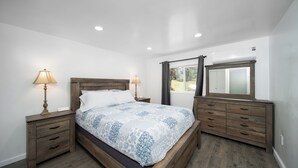 Une chambre à coucher avec un lit en bois, deux tables de chevet avec des lampes, une commode et une fenêtre avec des rideaux.