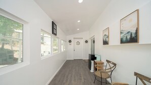 Un couloir avec un plancher en bois, des murs blancs et des œuvres d’art encadrées. On y trouve deux chaises en bois et une petite table.