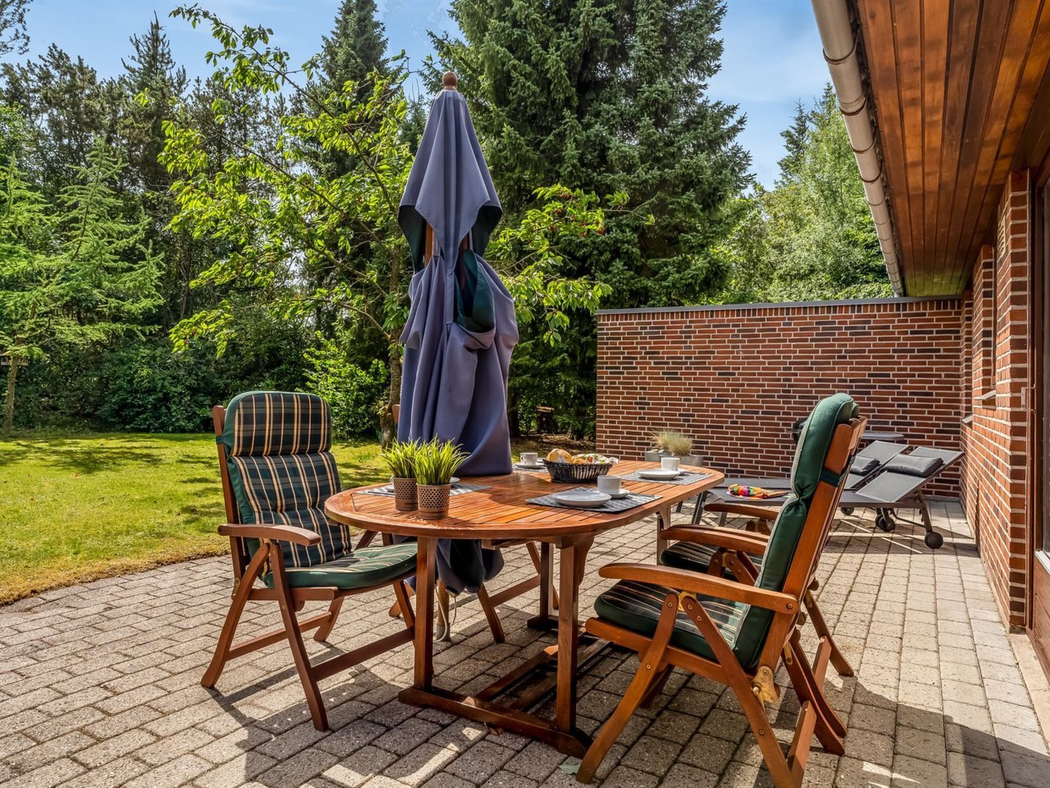 An outdoor patio with a brick wall, wooden furniture, and a table set for dining.