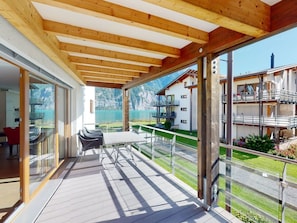 A covered outdoor area with a table and chairs, a glass door leading to a room, and a view of a mountain and lake. - Walensee House & Apartments, (Unterterzen), by Interhome (Unterterzen)
