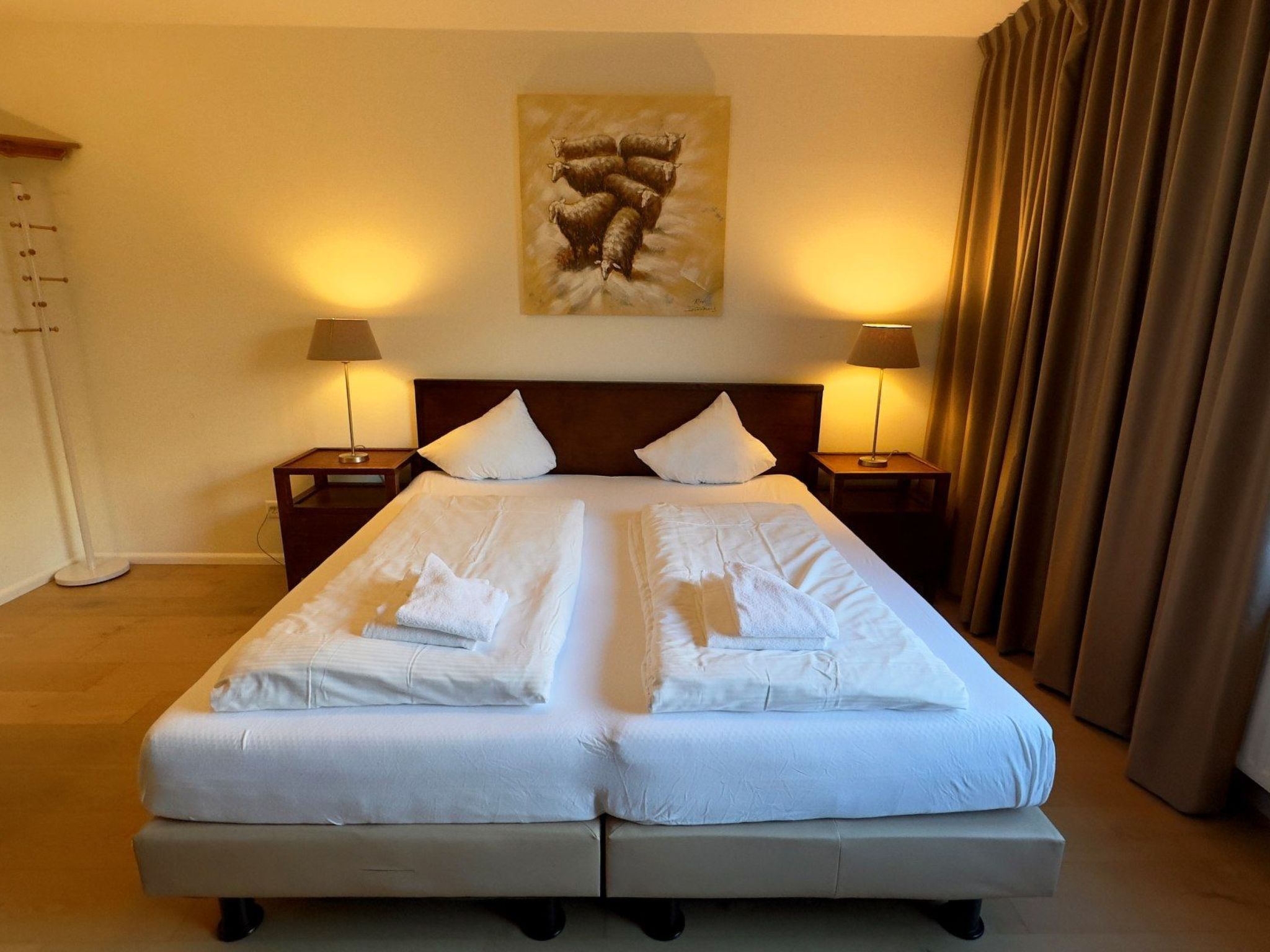 Une chambre d’hôtel avec un grand lit, deux tables de chevet, des lampes, un tableau au mur et un rideau.
