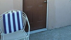 Una puerta marrón con el número 2 en la pared, una silla de metal con cojín a rayas y una reja de metal.