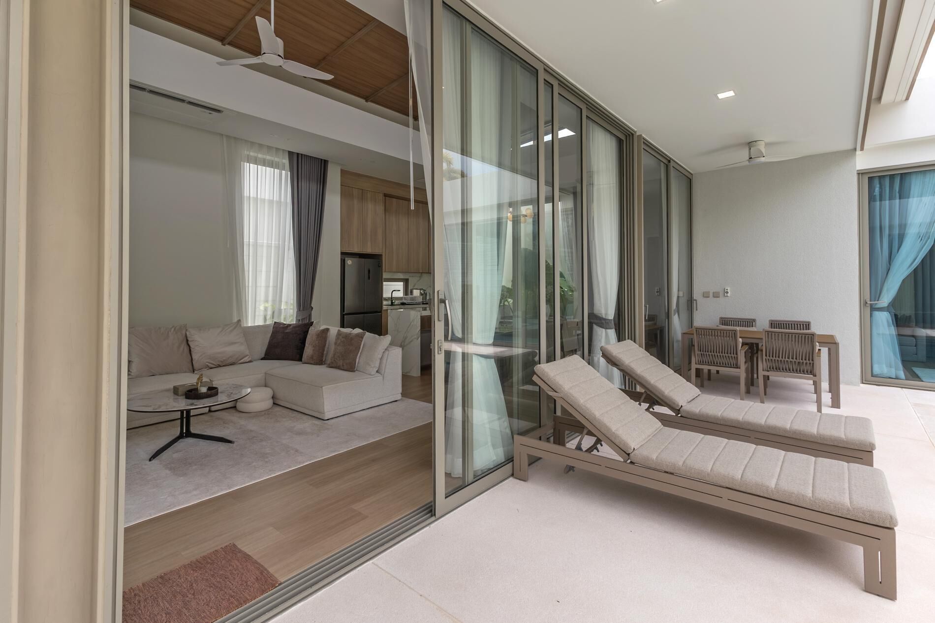 A modern living room with a sofa, a glass wall, a dining area with a table and chairs, and a lounge area with a bench.