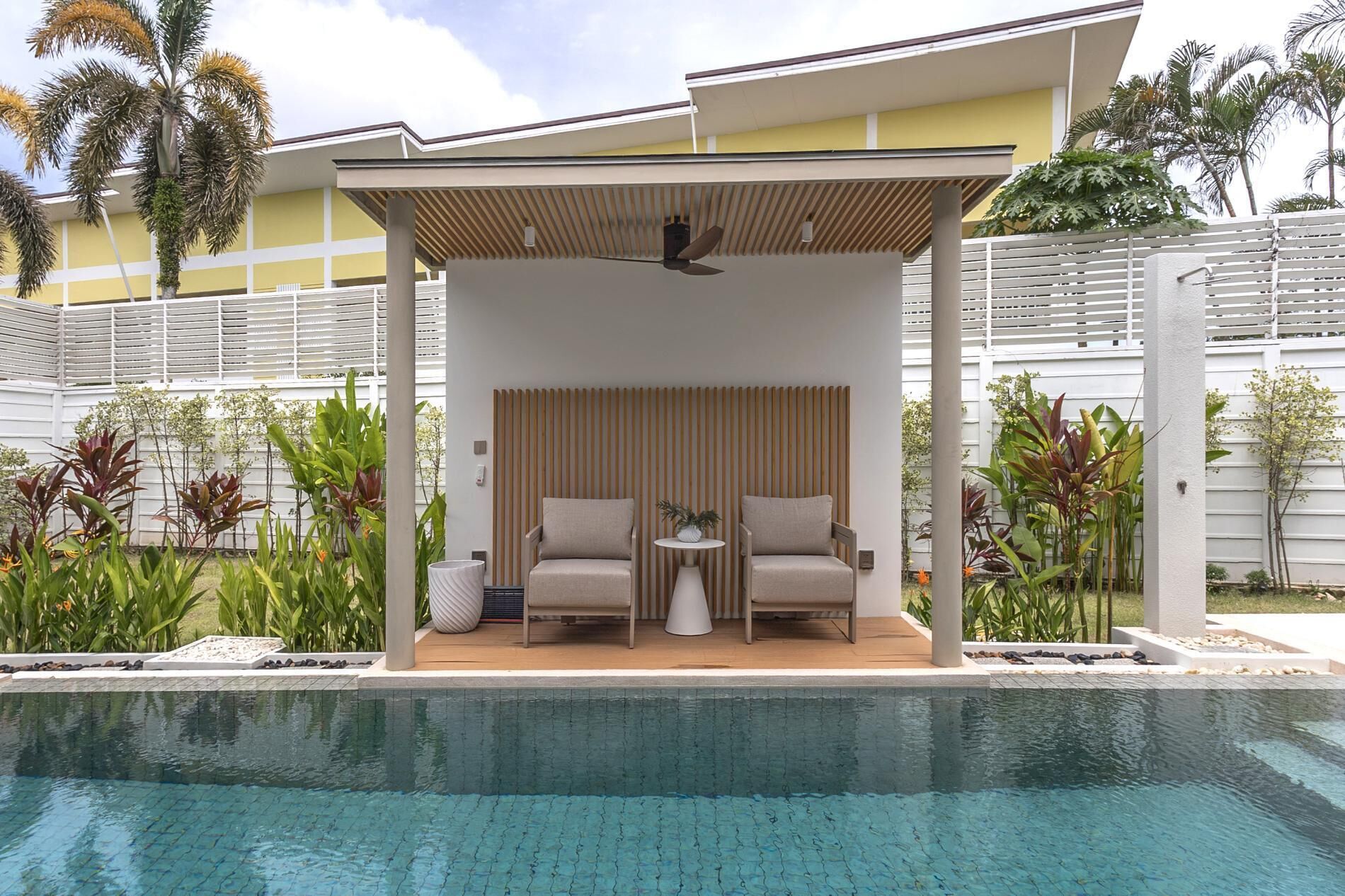 Un espace aménagé au bord de la piscine, avec deux chaises, une petite table et un ventilateur de plafond.