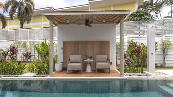 Un espace aménagé au bord de la piscine, avec deux chaises, une petite table et un ventilateur de plafond.