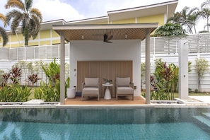 Un espace aménagé au bord de la piscine, avec deux chaises, une petite table et un ventilateur de plafond.