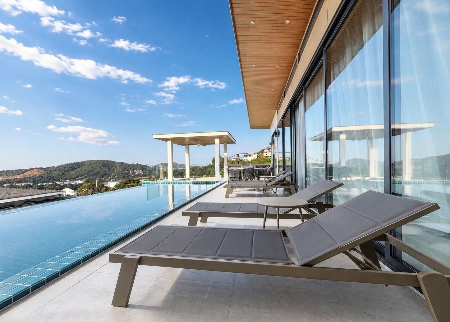 A modern outdoor pool area with lounge chairs and a pergola, overlooking a scenic landscape.