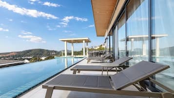 Un área moderna de piscina al aire libre con sillas de descanso y una pérgola, con vistas a un paisaje pintoresco.