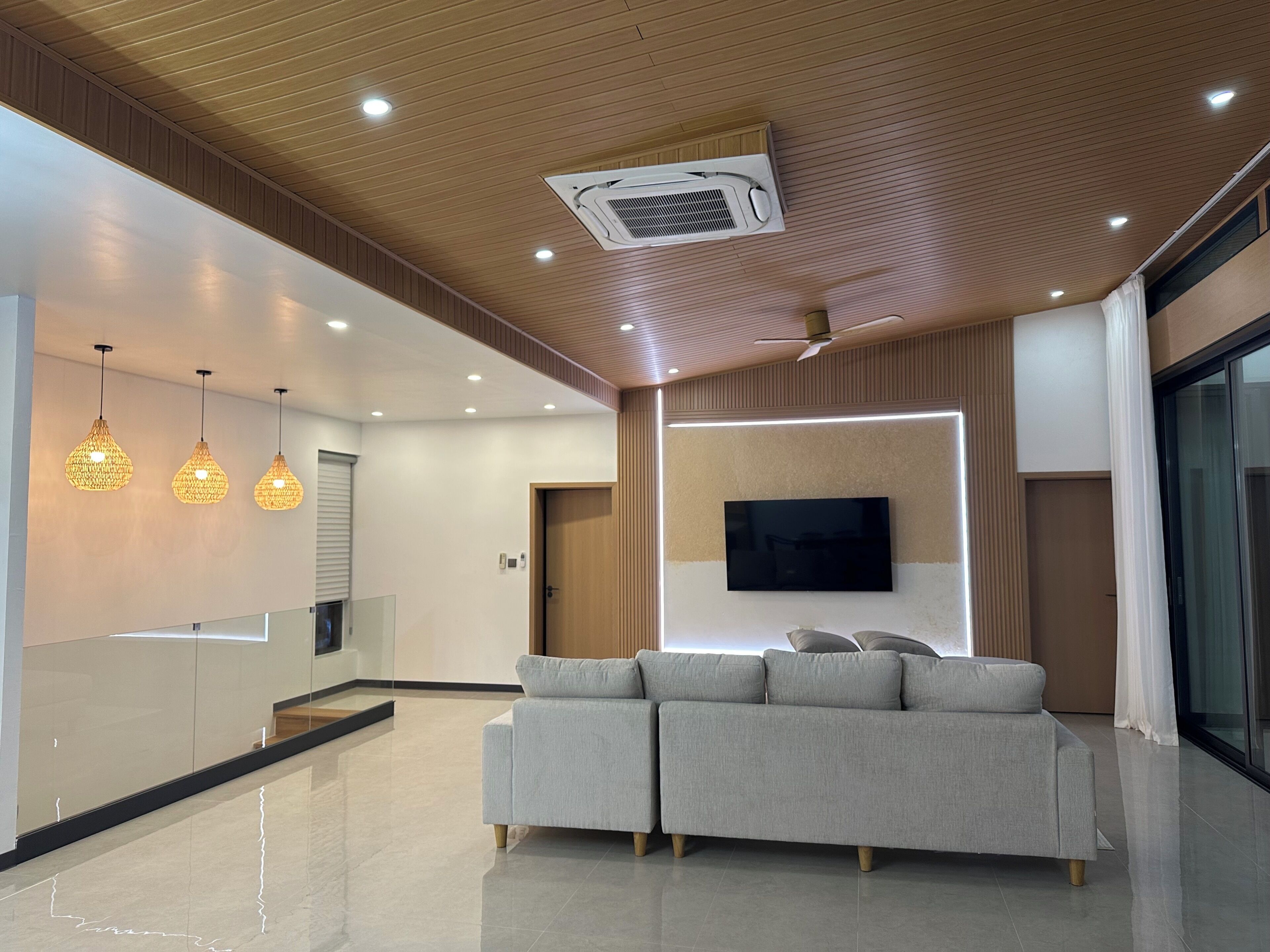 A modern living area with a sofa, pendant lights, a flat-screen TV, and a ceiling fan.