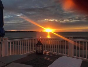 Auringonlaskunäkymä parvekkeelta, jossa on kaide, lyhty ja näkymä merelle.