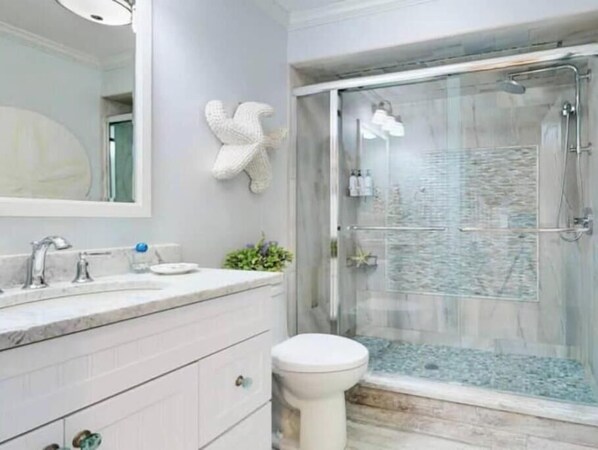 A bathroom with a marble sink, a white toilet, and a glass-enclosed shower with a pebble floor.