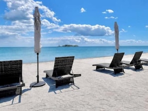 A beach with lounge chairs and umbrellas, a clear sky, and a distant island.