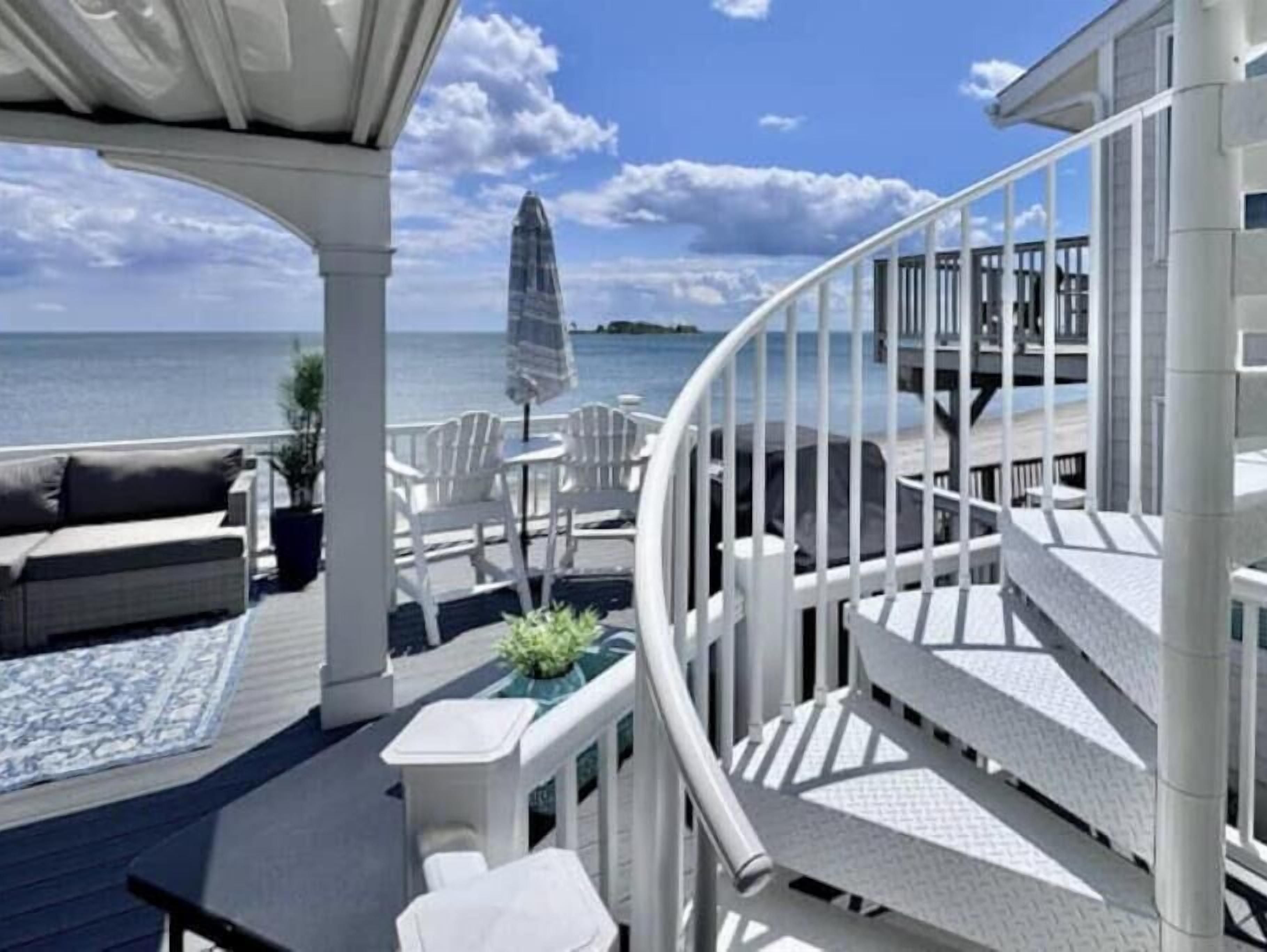 Une terrasse avec coin salon extérieur, un escalier en colimaçon et une vue sur la mer.