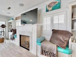 A living room with a fireplace, a television, and a seating area with cushions.