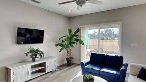A living room with a flat-screen TV, a large potted plant, a blue sofa, a white sofa, and a coffee table. - Beach Bliss - Hot Tub, Fenced Yard 3 Bedrooms in Panama City Beach (Panama City Beach)