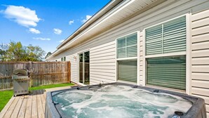 A hot tub on a wooden deck, a wooden fence, and a house with white siding and green shutters. - Beach Bliss - Hot Tub, Fenced Yard 3 Bedrooms in Panama City Beach (Panama City Beach)