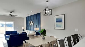 A modern living room with a sofa, dining table, chairs, and a ceiling fan. - Beach Bliss - Hot Tub, Fenced Yard 3 Bedrooms in Panama City Beach (Panama City Beach)
