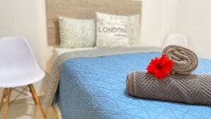 Een net opgemaakt bed met een blauwe quilt, een opgerolde handdoek en een rode bloemdecoratie.