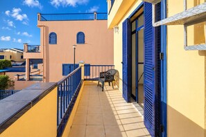 Ein Balkon mit Stuhl und Tisch, einem blauen Geländer und einem Gebäude mit blauen Fensterläden.