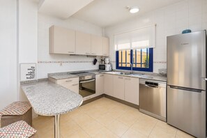 Eine moderne Küche mit einem Edelstahl-Kühlschrank, einem Einbauofen, einer Mikrowelle und einem Geschirrspüler. Ein Fenster mit blauen Fensterläden bietet Blick auf umliegende Gebäude.