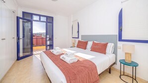 Habitación de hotel con cama, mesita de noche, lámpara y vista a través de un ventanal.