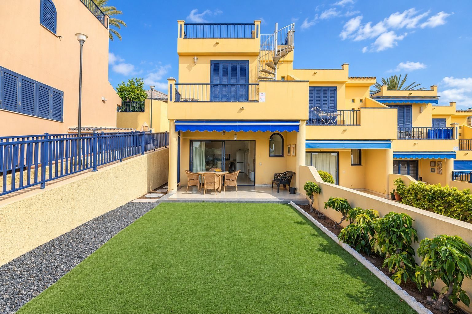 A two-story residential building with a covered patio, a small lawn, and a blue railing.
