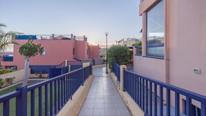 Un pasillo con suelo de baldosas, barandas azules y edificios con balcones.