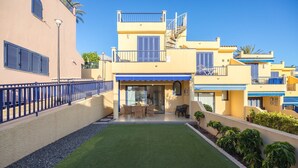 Un edificio moderno de dos plantas con techo plano, un patio cubierto y un pequeño jardín.