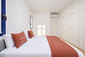 Une chambre à coucher avec un lit, des murs blancs, une porte bleue et une armoire.