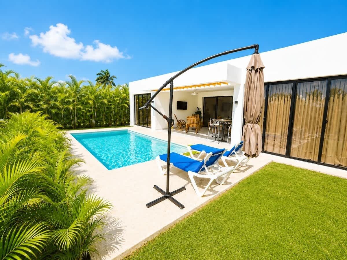 Un área de piscina moderna al aire libre, con una piscina azul cristalina, sillas de descanso y una pérgola con un columpio.