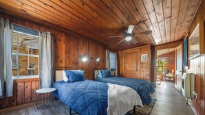 A wooden cabin room with two beds, a ceiling fan, and a small table. - Pet-Friendly Getaway Downtown (Hot Springs)