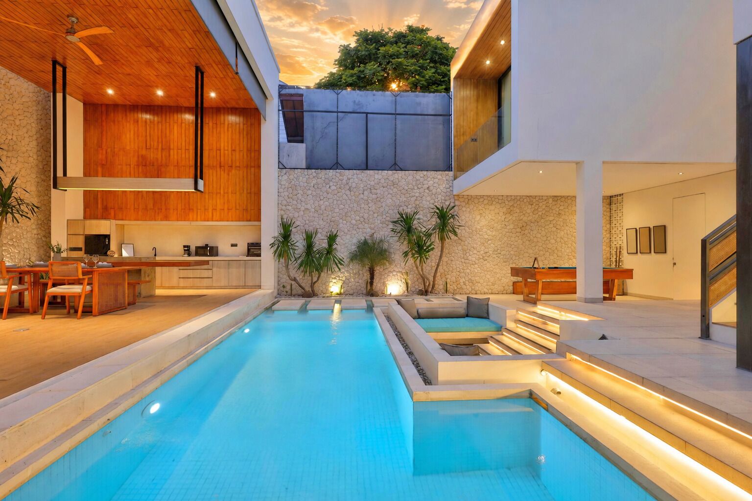 A modern indoor pool with a stone wall and wooden ceiling, surrounded by seating and a pool table.