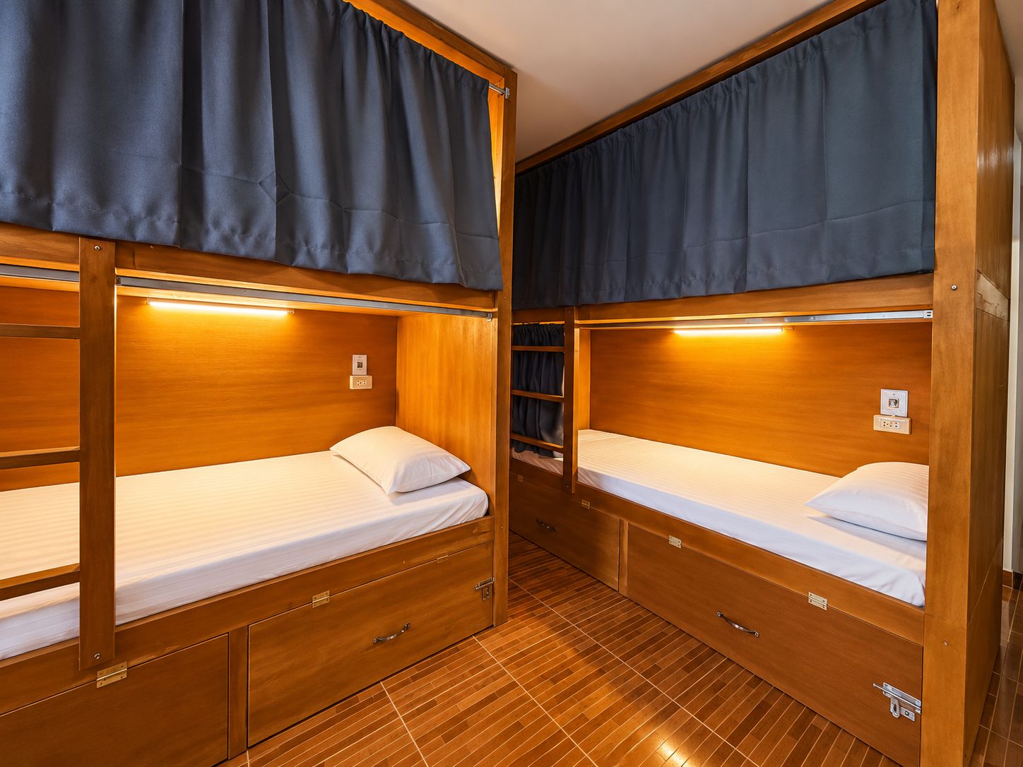 A compact, well-lit room with two bunk beds, each with a small drawer and a bedside table.