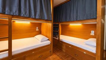 A compact, well-lit room with two bunk beds, each with a small drawer and a bedside table.