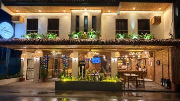 A hotel with a reception area, outdoor seating, and a well-lit entrance.