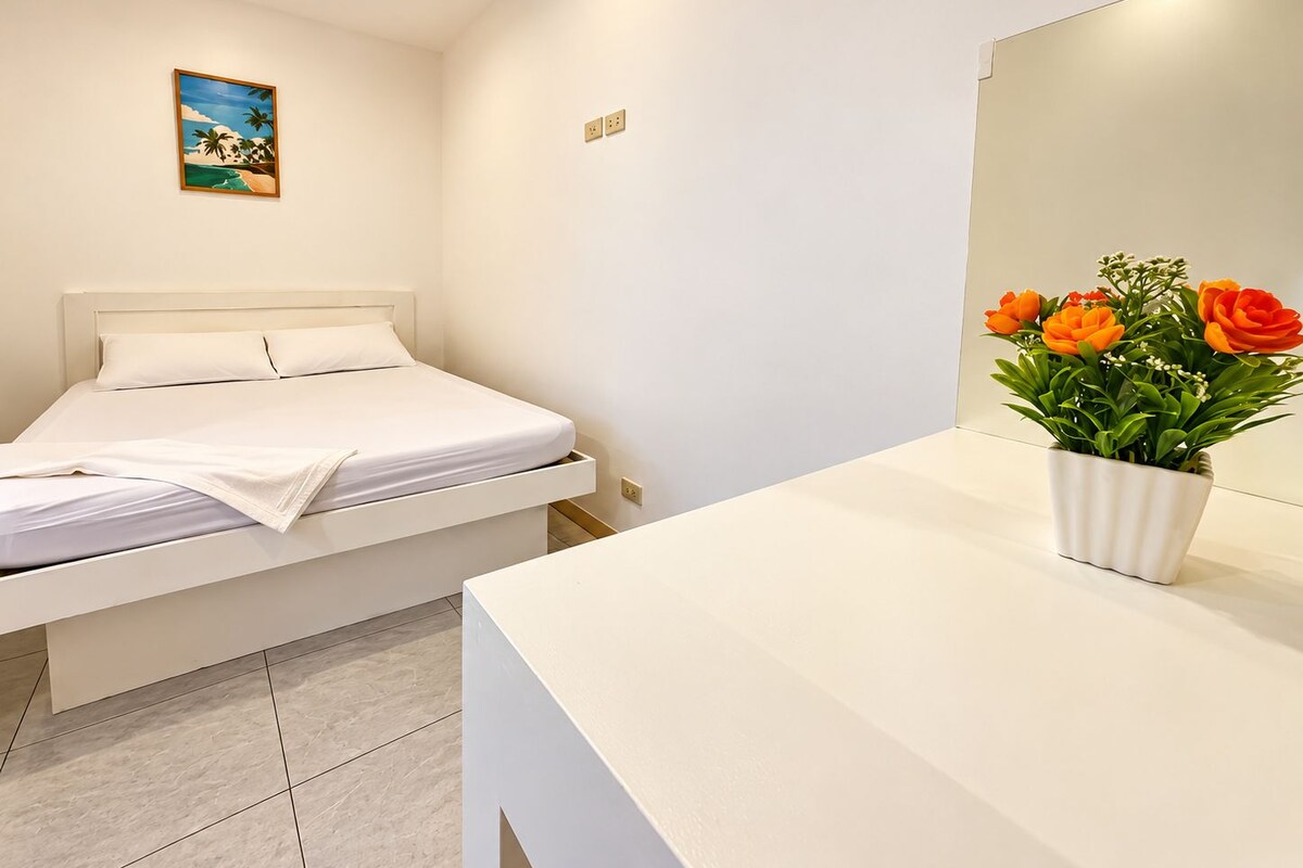 Une chambre à coucher avec un lit, une table de chevet, une plante en pot et un tableau accroché au mur.