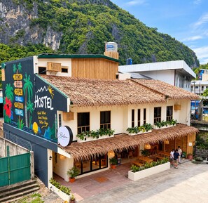 Une auberge de jeunesse avec un toit de chaume, une fresque murale faisant la publicité des chambres, du bar, du café et des services de voyage, et une vue sur un paysage montagneux.