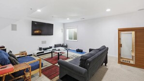 A modern living room with a flat-screen TV, exercise equipment, a sofa, and a dining area. - Spacious 5BR house in tranquil Wash DC community has Sauna, fitness, and more (Washington)