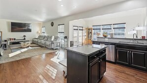 A spacious living area with a sofa, a coffee table, and a TV. The kitchen features a large island with a sink and black cabinets. - Spacious 5BR house in tranquil Wash DC community has Sauna, fitness, and more (Washington)