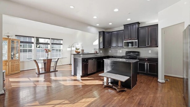 A modern kitchen with dark cabinetry, stainless steel appliances, and a wooden dining table with chairs. - Spacious 5BR house in tranquil Wash DC community has Sauna, fitness, and more (Washington)