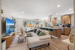 A modern living room with a sofa, a TV, and a kitchen area with wooden cabinets and a central island.