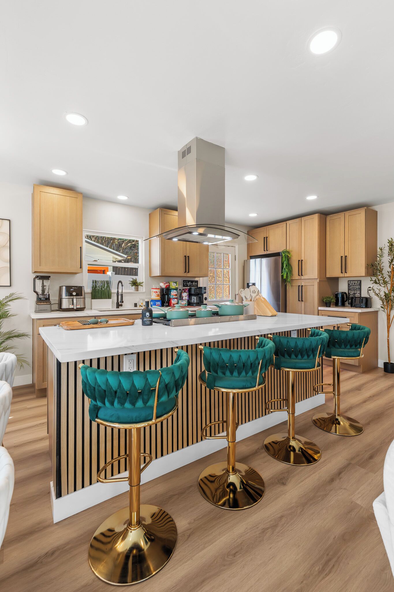 A modern kitchen with a central island, bar stools, wooden cabinets, and a stainless steel refrigerator.